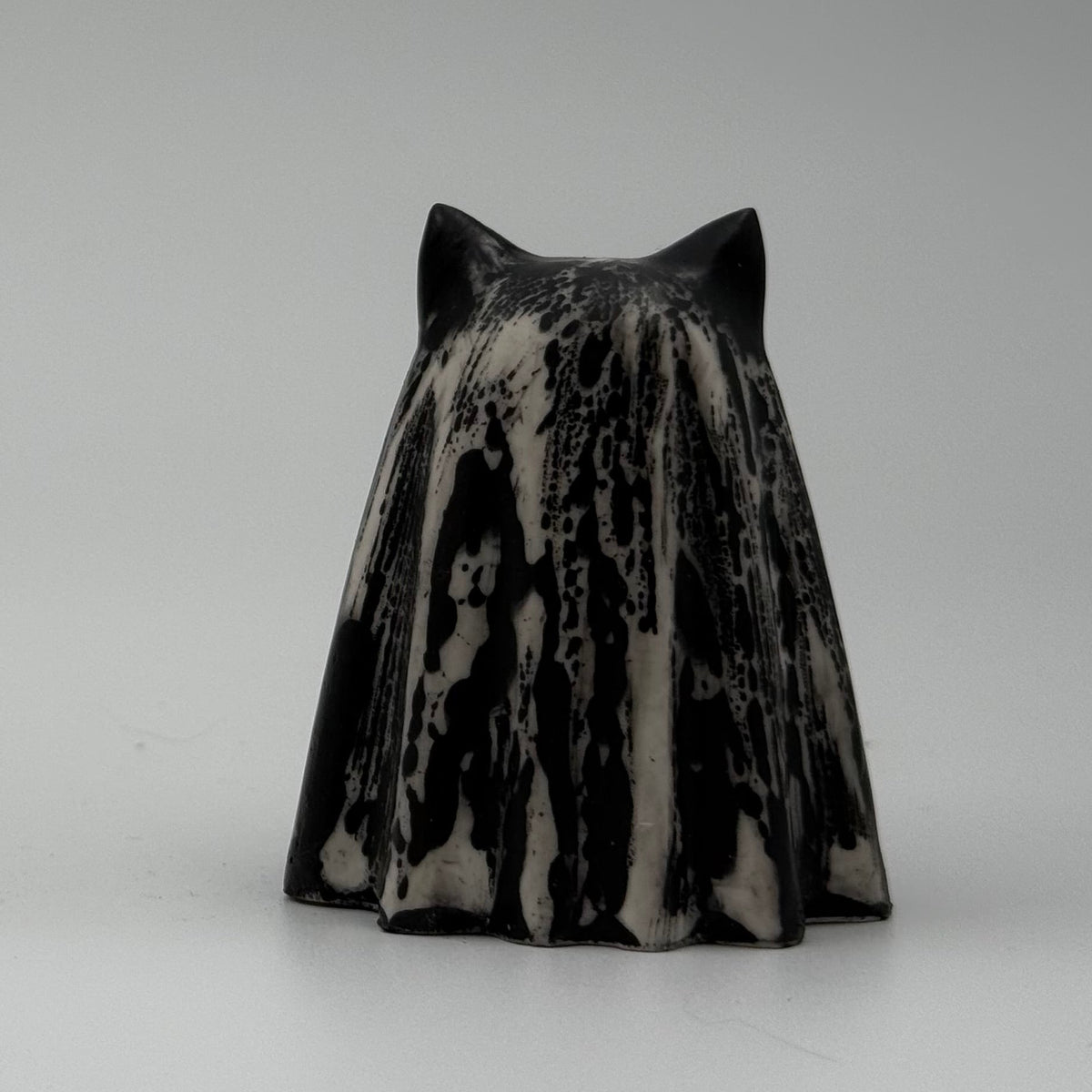 An ivory coloured ghost cat figurine with dramatic black, bark like patterning made by The Nordic Ghost Merchants. Side view.