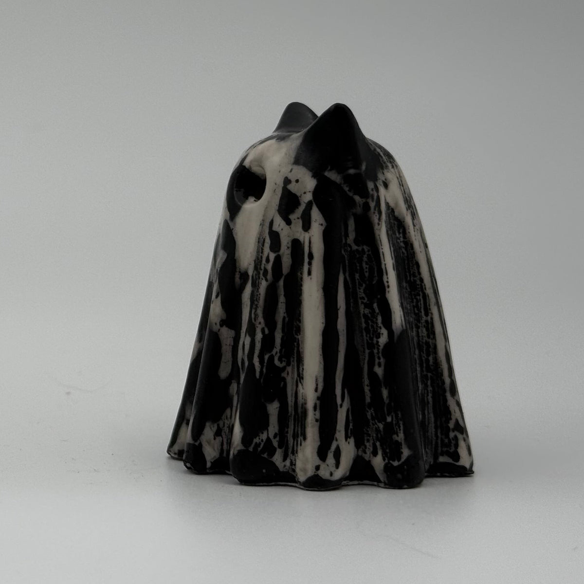 An ivory coloured ghost cat figurine with dramatic black, bark like patterning made by The Nordic Ghost Merchants. Side view.