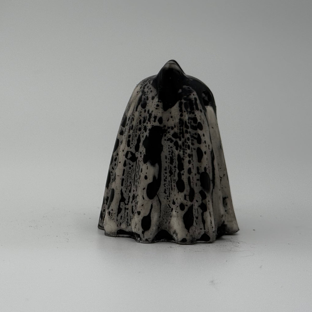 A small black and white ghost cat figurine made by The Nordic Ghost Merchants. Side view.
