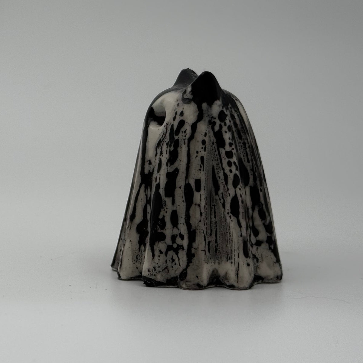 A small black and white ghost cat figurine handmade by The Nordic Ghost Merchants. The pattern resembles rain running down a window. Sideview