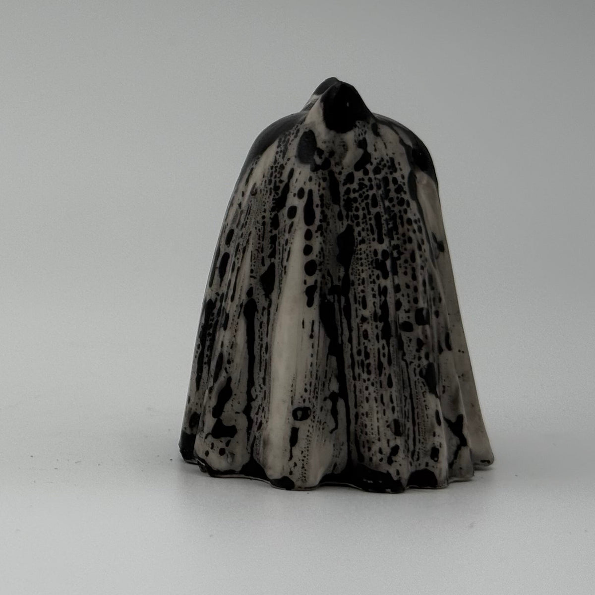 A small black and white ghost cat figurine. The black marks resemble rain dripping down a window. Handmade by The Nordic Ghost Merchants. Side view.