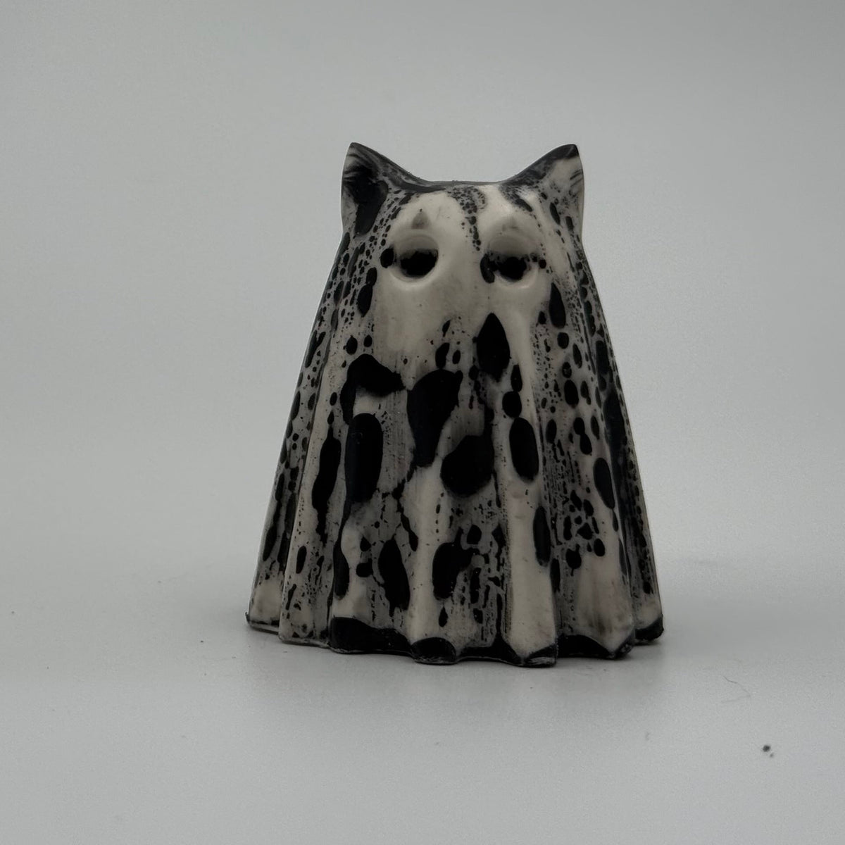 An ivory coloured ghost cat figurine with dramatic black, bark like patterning, made by The Nordic Ghost Merchants. Front view.