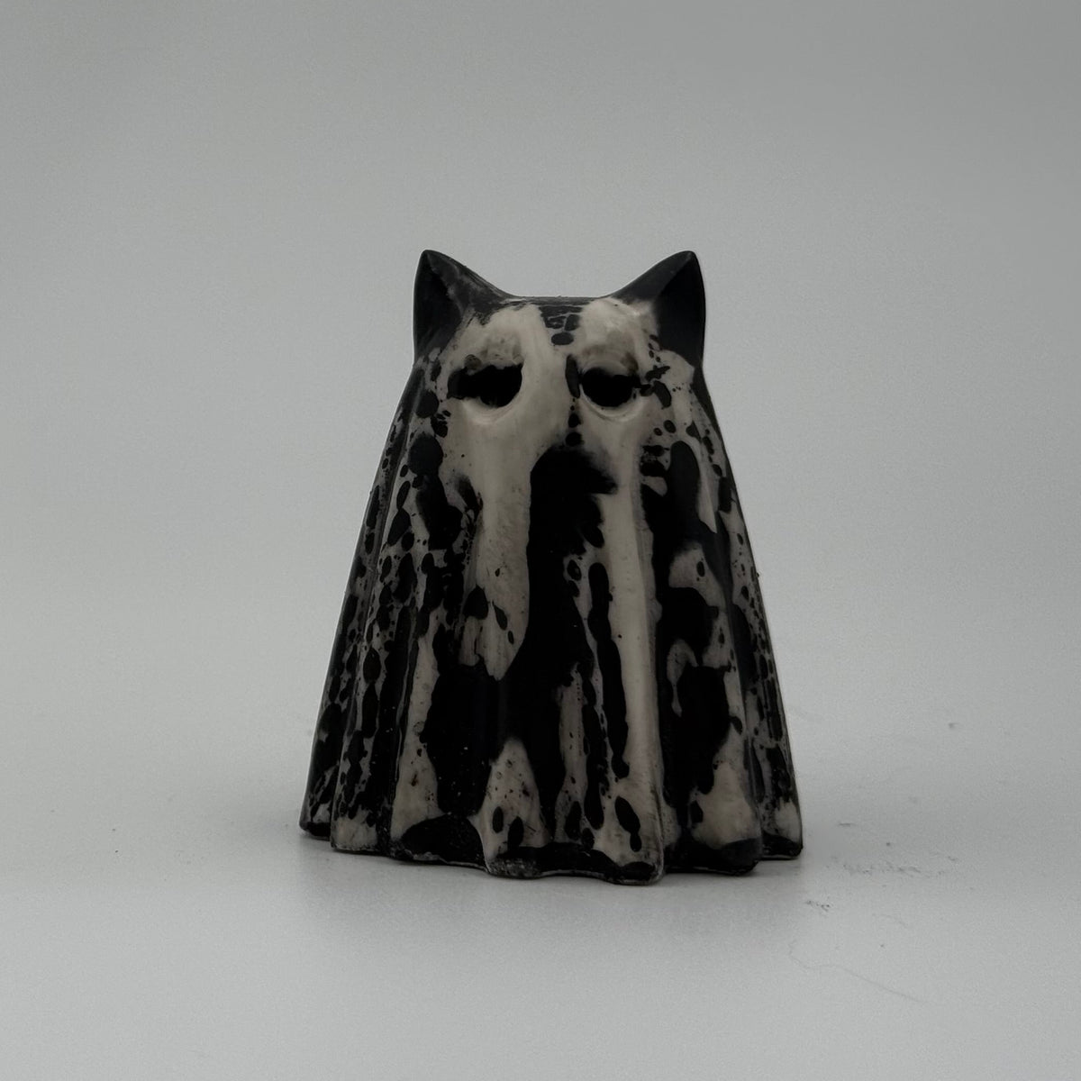 A small black and ivory coloured ghost cat figurine by The Nordic Ghost Merchants. Front view