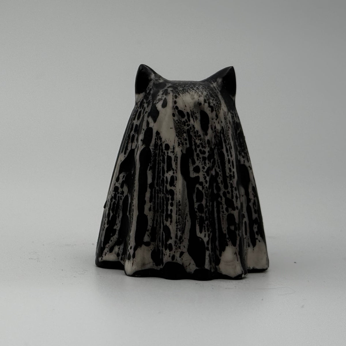 A small black and white ghost cat figurine made by The Nordic Ghost Merchants. The pattern resembles bark. Rear view.