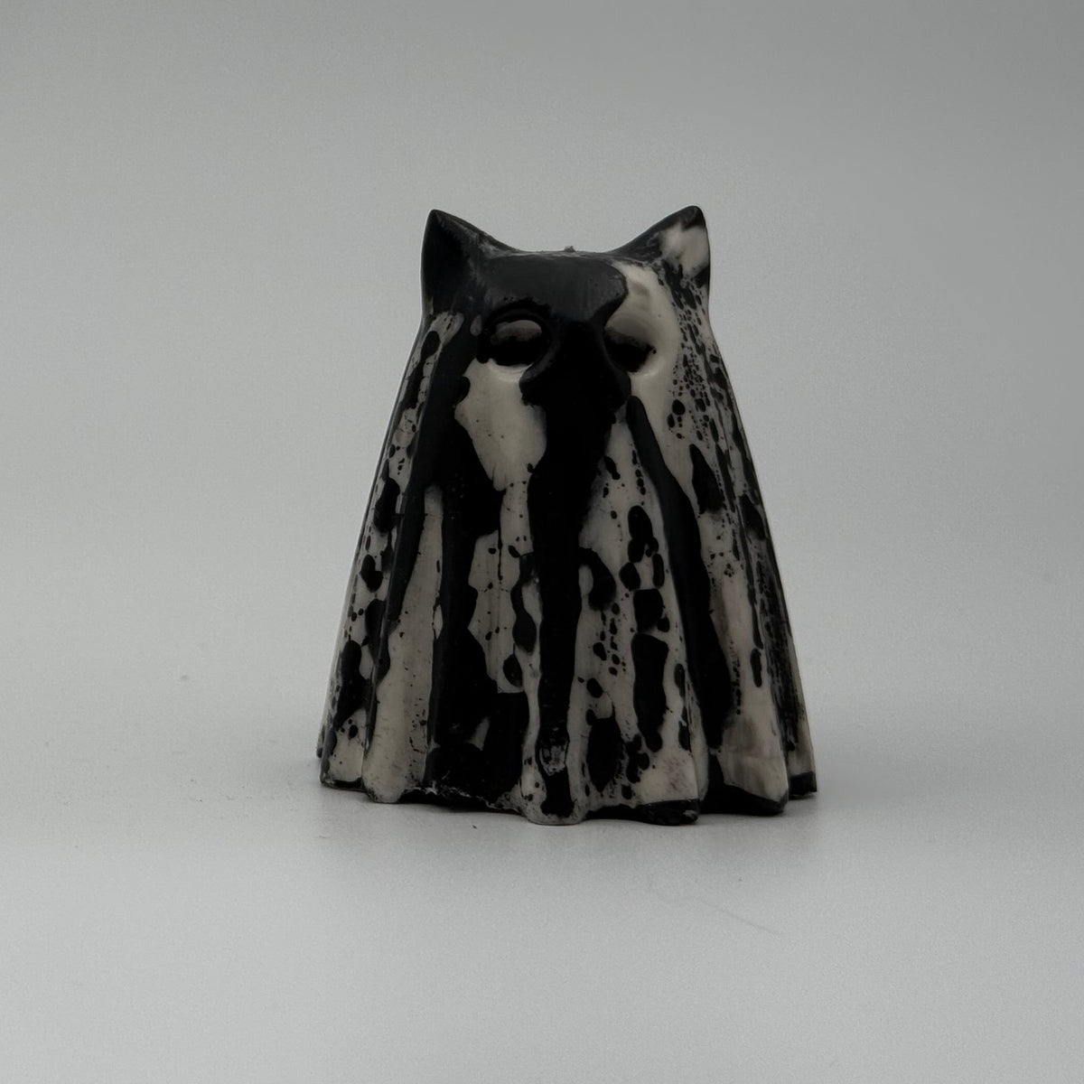 An ivory coloured ghost cat figurine with dramatic, black, bark like patterning, made by The Nordic Ghost Merchants. Front view