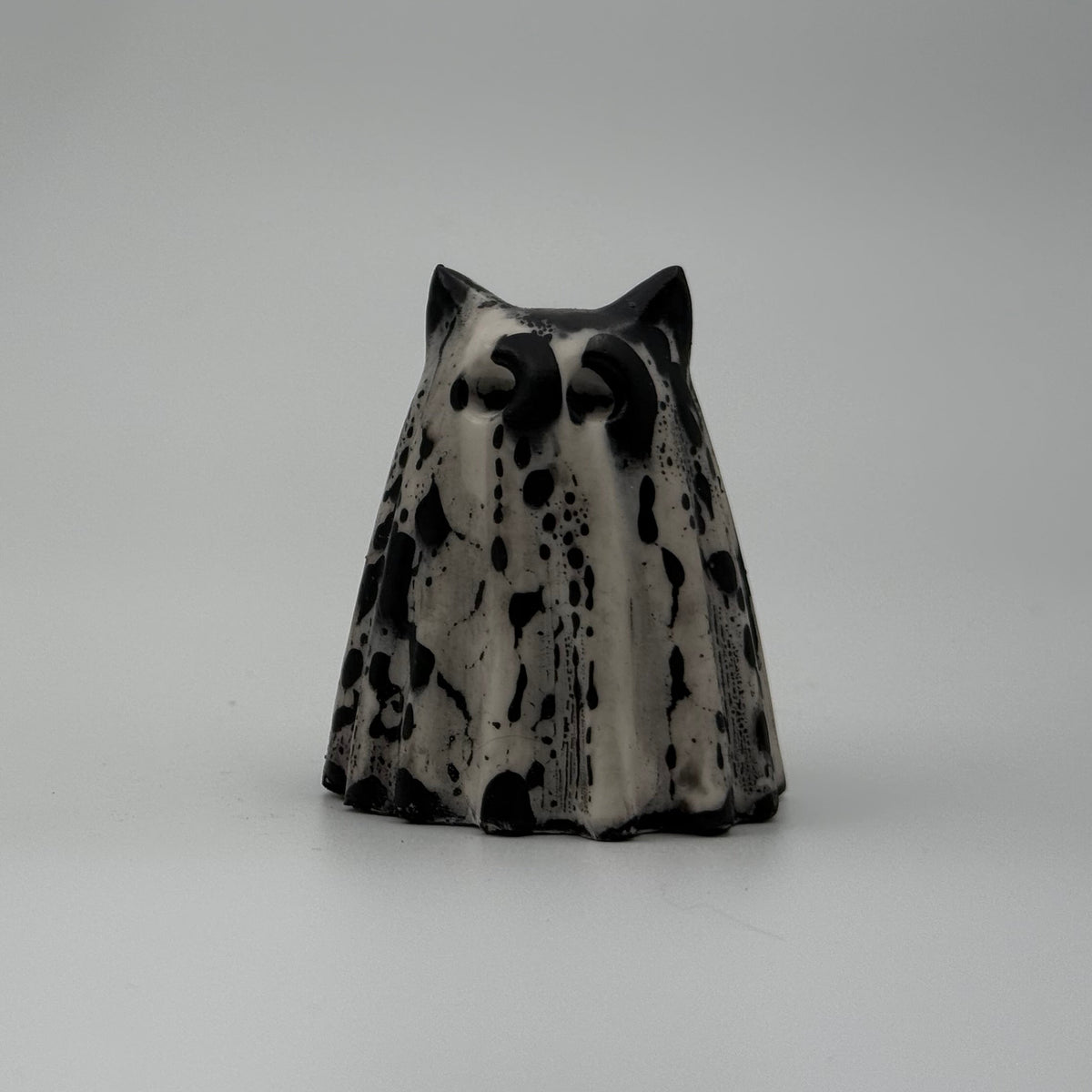 An ivory coloured ghost cat figurine with dramatic black, bark like patterning, by The Nordic Ghost Merchants. Front view.