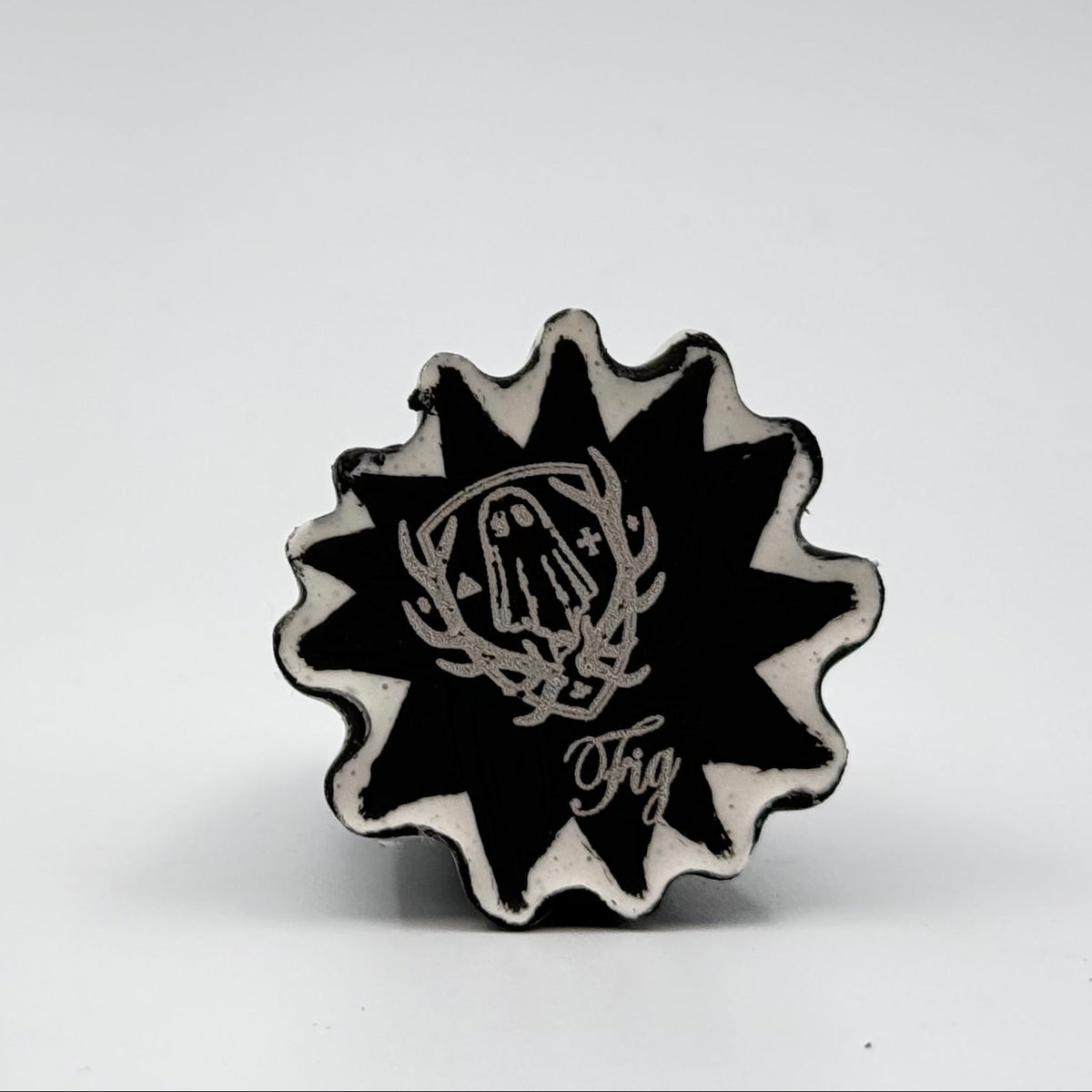 A handmade ghost cat figurine by The Nordic Ghost Merchants. The image is of the base of the ghost ornament, painted black and engraved with the brand logo - a coat of arms with a sheet ghost in the centre.