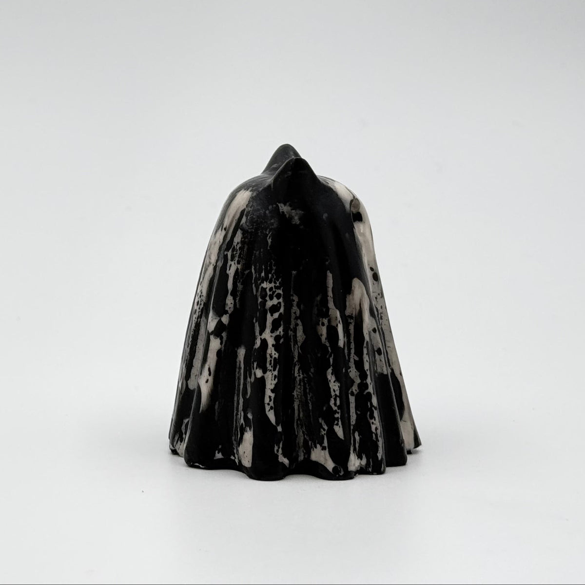 A handmade ghost cat figurine by The Nordic Ghost Merchants. The ghost ornament is bone white with black, bark like patterning. Side view on a grey studio background.