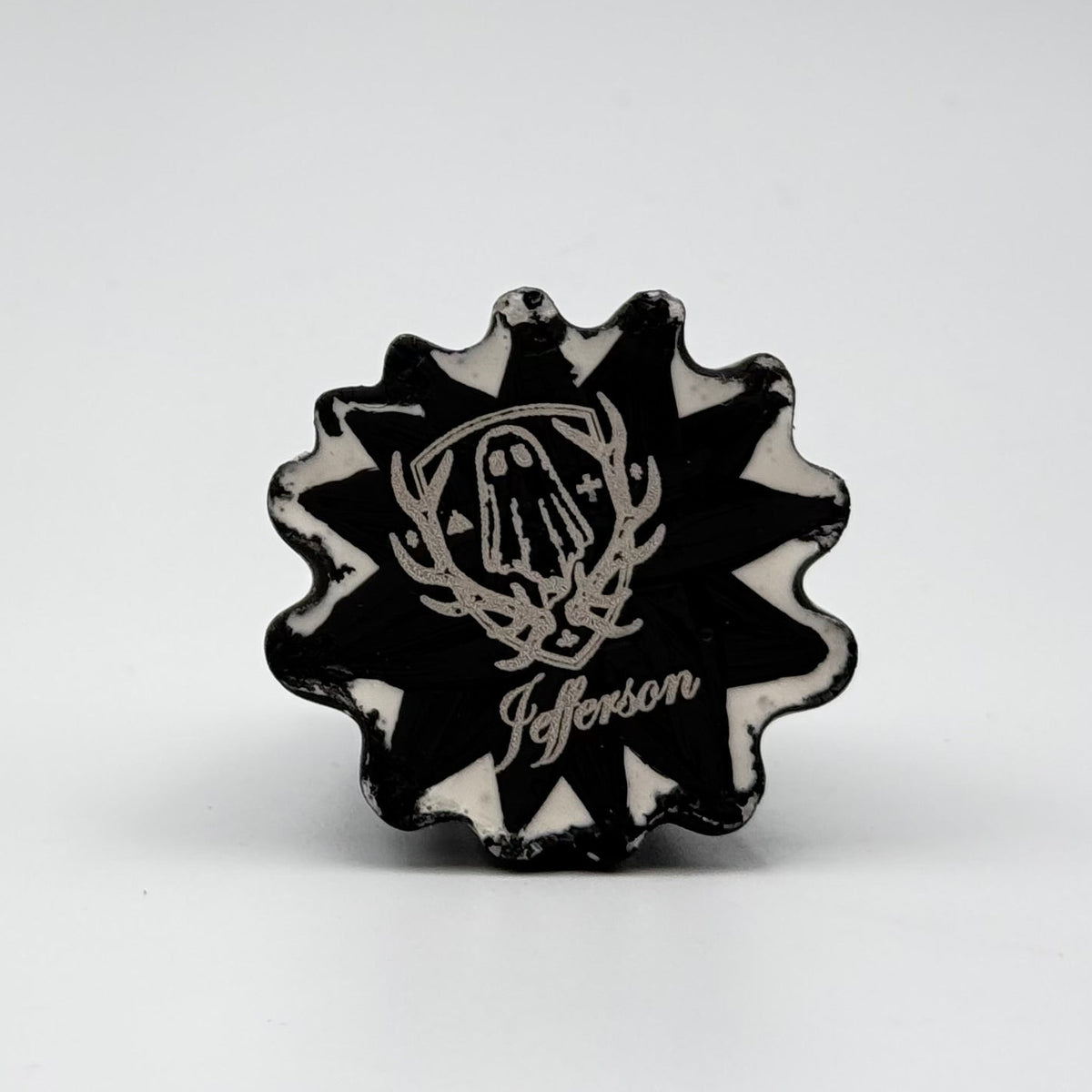 A handmade ghost cat figurine by The Nordic Ghost Merchants. The image is of the base of the ghost ornament, painted black and engraved with the logo of the brand - a coat of arms with a sheet ghost in the centre.
