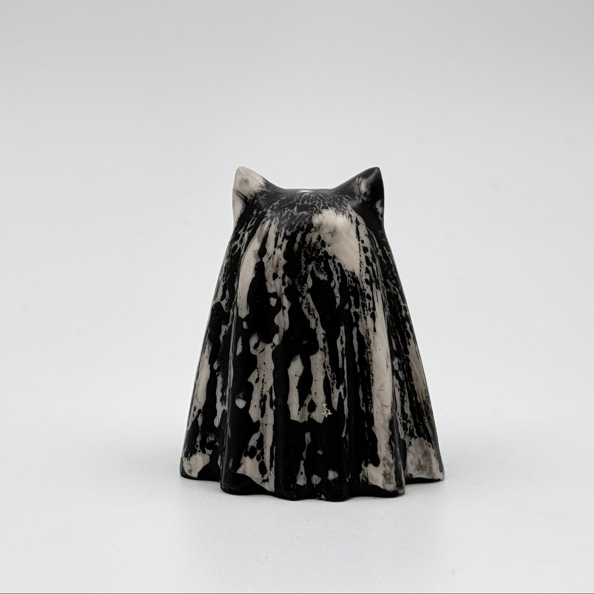 A handmade ghost cat figurine by The Nordic Ghost Merchants. The ghost ornament is bone white with a black, bark like pattern. Rear view on a grey studio background.