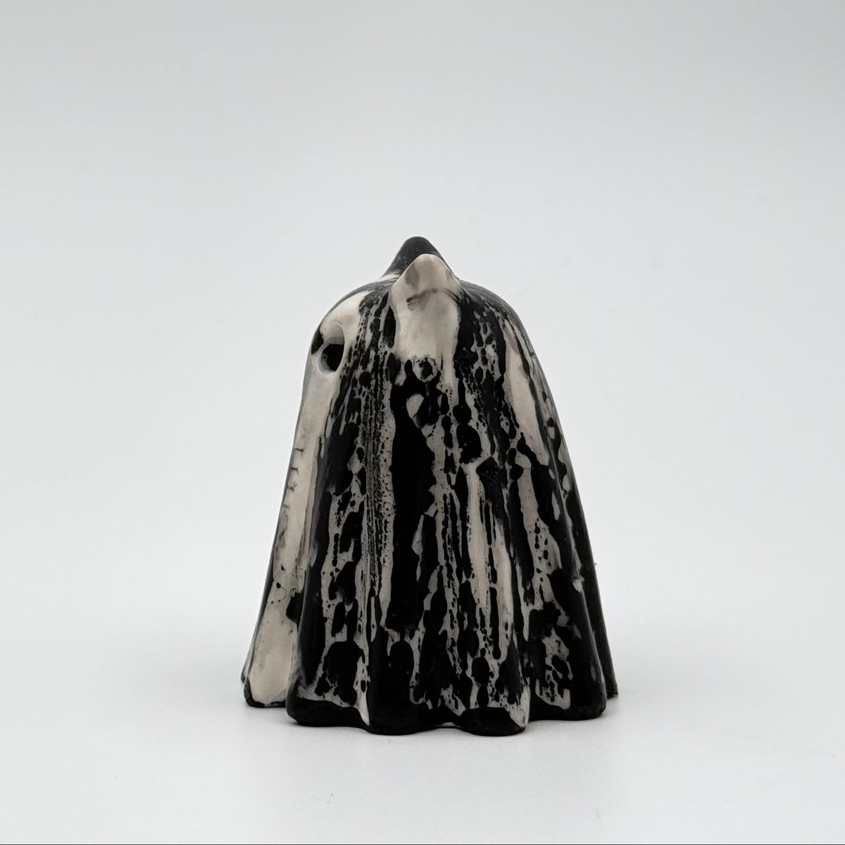 A handmade ghost cat figurine by The Nordic Ghost Merchants. The ghost ornament is bone white with a black, bark like pattern. Side view on a grey studio background.
