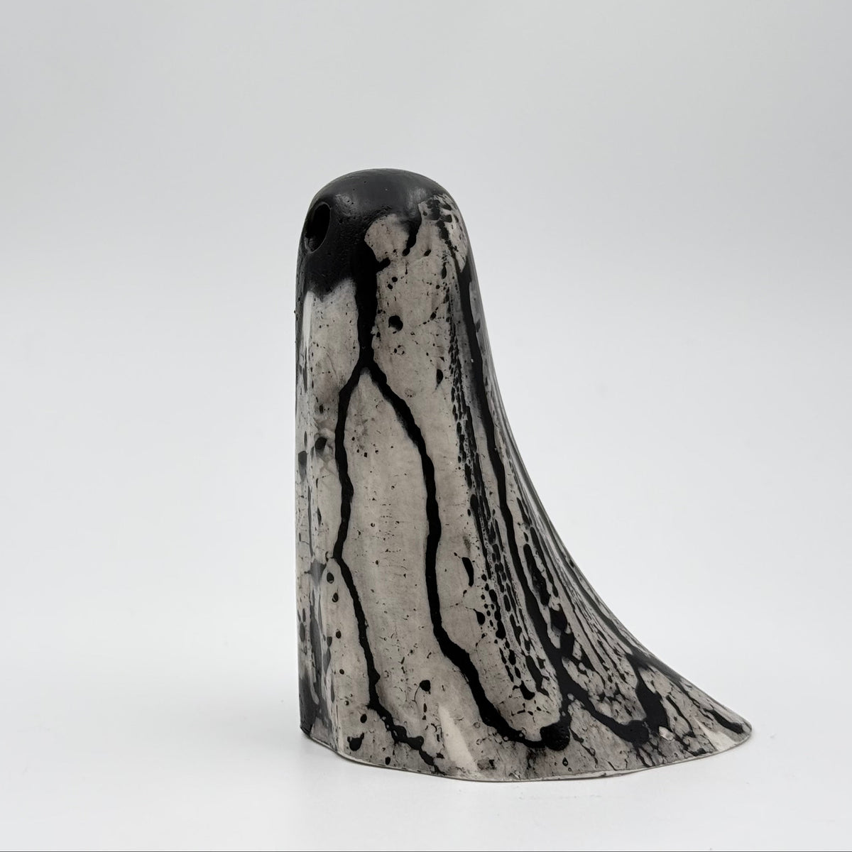 A handmade ghost figurine made by The Nordic Ghost Merchants in Denmark. The ghost is bone white with black, bark like patterning. Side view on a grey studio background.