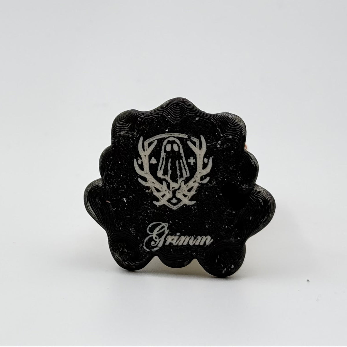 A hand painted folklore figurine made by The Nordic Ghost Merchants in Denmark. The image shows the base of the folklore ornament, painted black and engraved with the brand logo - a coat of arms with a sheet ghost in the centre.