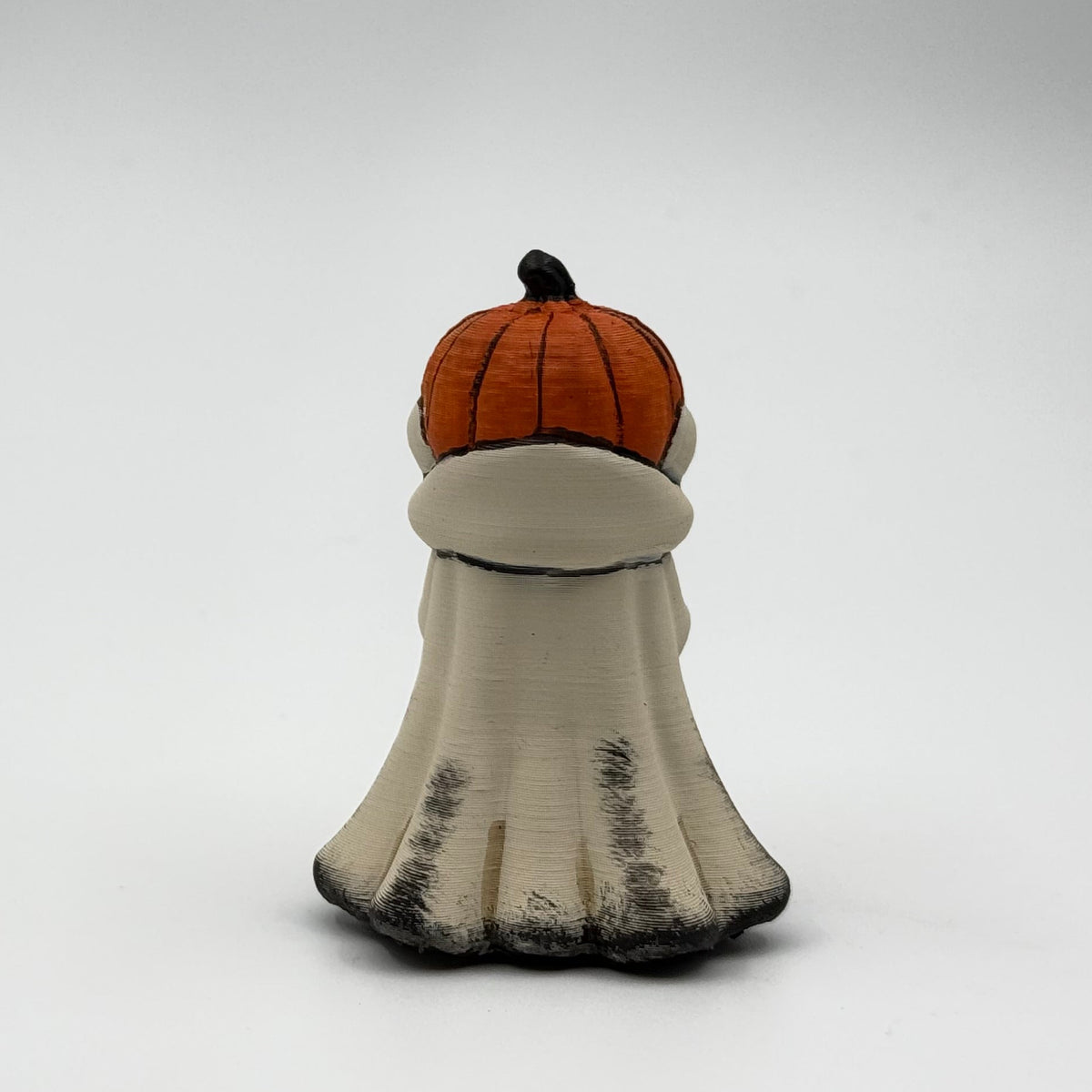 A hand painted folklore figurine made by The Nordic Ghost Merchants in Denmark. The figurine has a carved pumpkin head and is robed in cream cloth while he clutches an autumn leaf. Front view on a grey studio background.