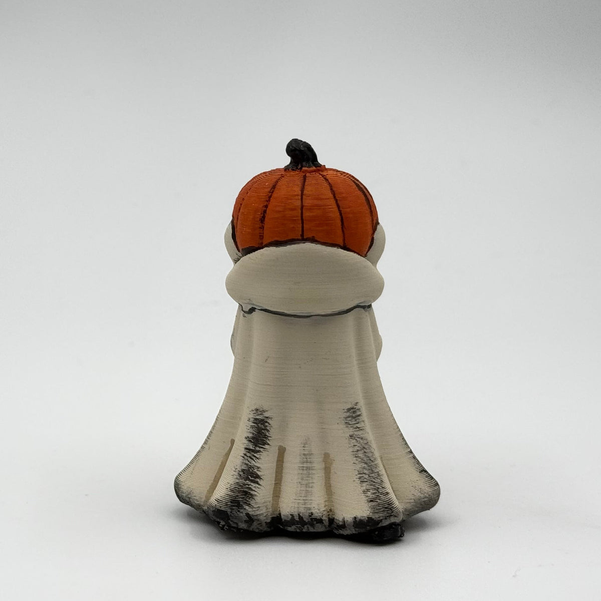 A hand painted folklore figurine made by The Nordic Ghost Merchants in Denmark. The figurine has a carved pumpkin head and is robed in cream cloth while he clutches an autumn leaf. Rear view on a grey studio background.