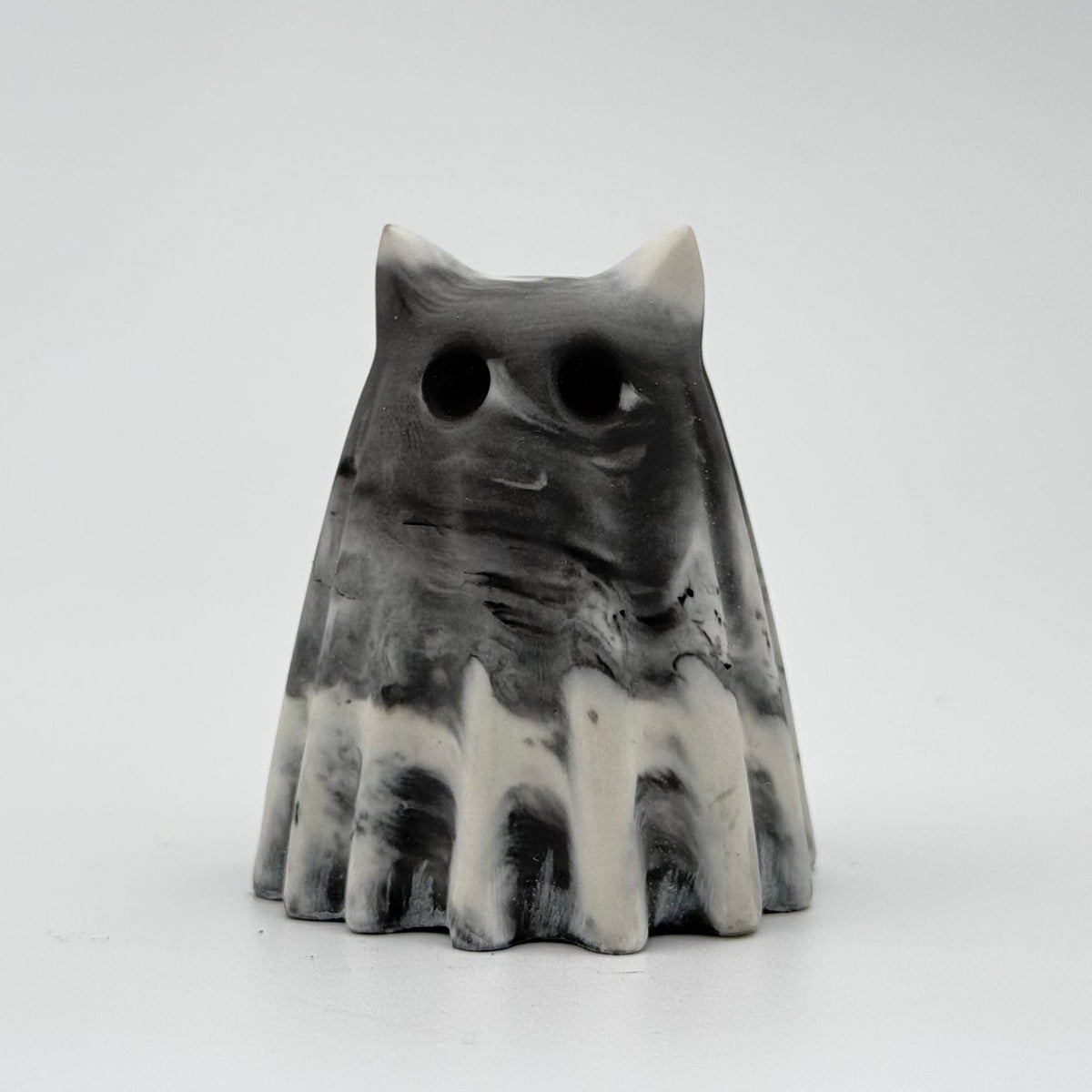 A grey and white marbled handmade ghost cat figurine by The Nordic Ghost Merchants. The colours are in a smoky or fog-like pattern. Front view on a grey studio background.