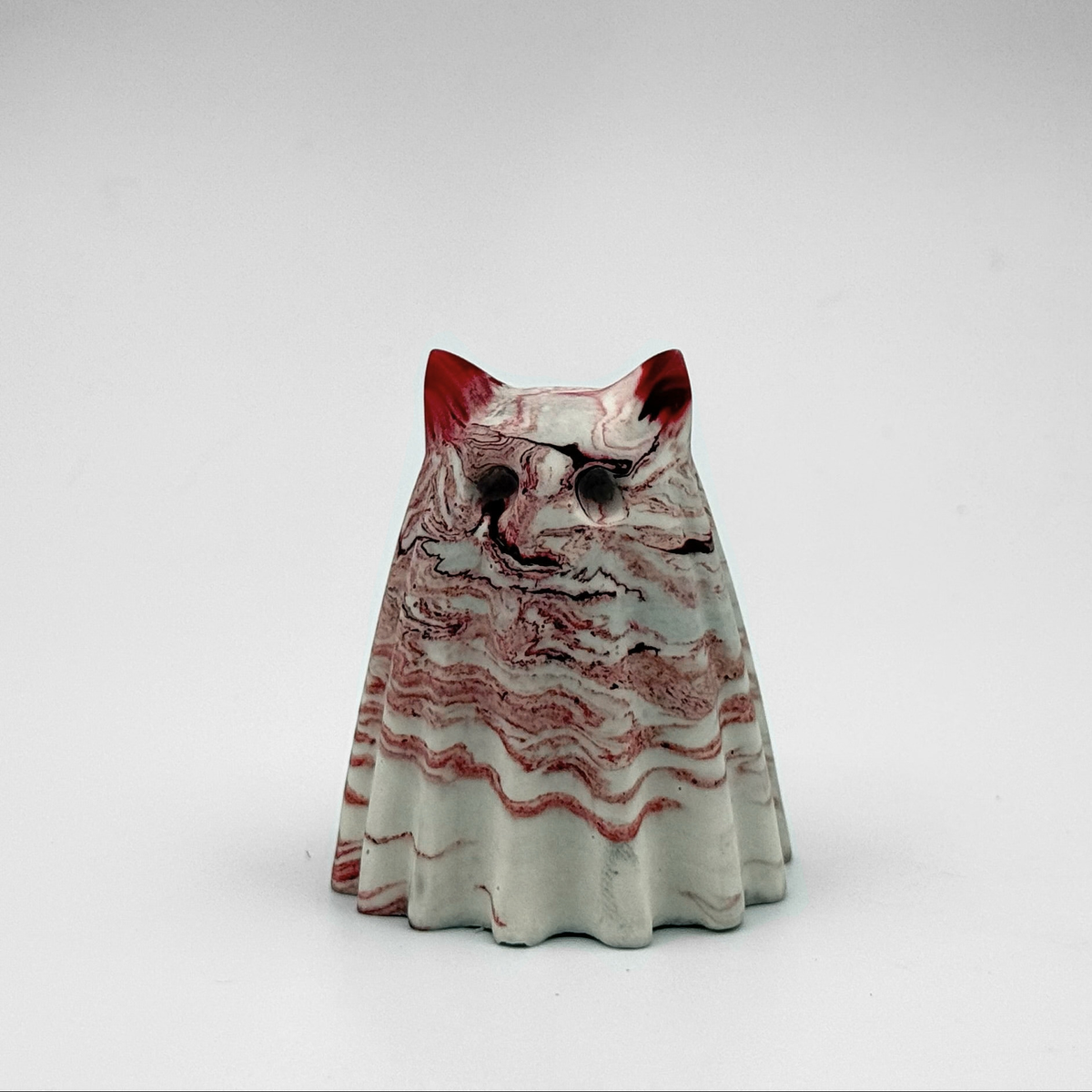 A small grey and white marbled ghost cat figurine with red ripples throughout. Handmade by The Nordic Ghost Merchants. Front view