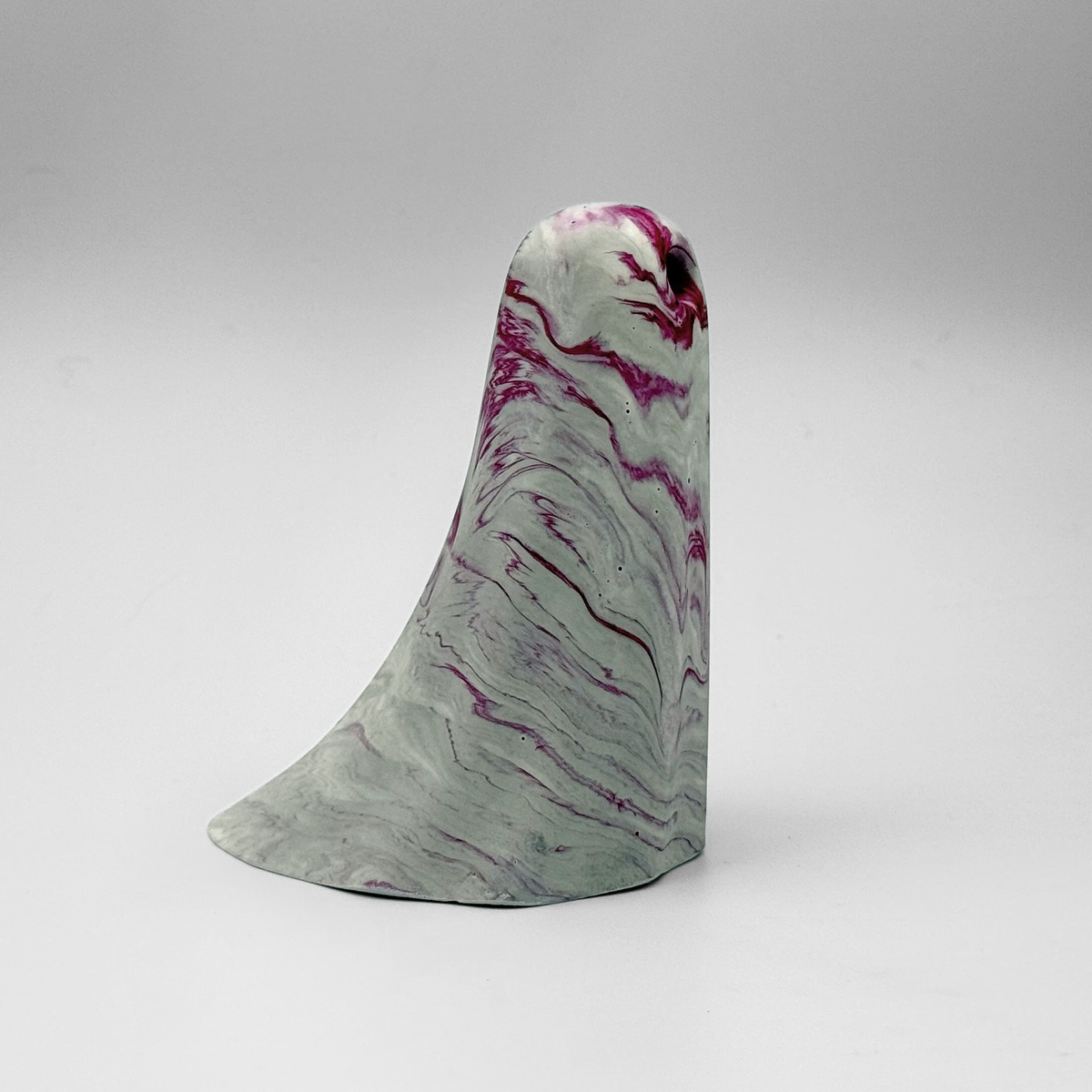 A white and grey marbled handmade ghost figurine by The Nordic Ghost Merchants. The ghost has cerise pink ripples running through it. Side view on a grey studio background.