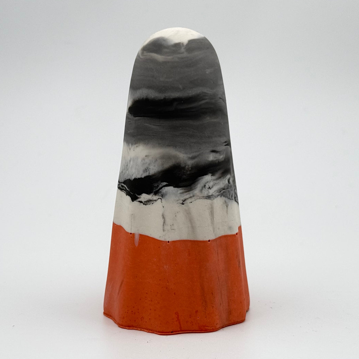 A handmade ghost figurine made by The Nordic Ghost Merchants in Denmark. The body of the ghost is grey and white marbled. The bottom quarter is a pumpkin orange. Rear view on the grey studio background.