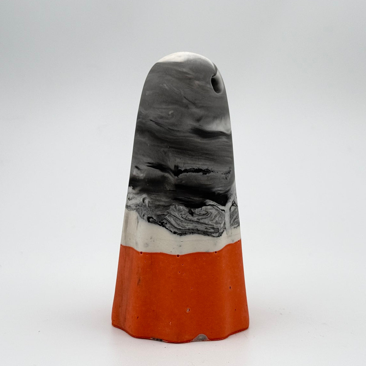 A handmade ghost figurine made by The Nordic Ghost Merchants in Denmark. The body of the ghost is grey and white marbled. The bottom quarter is a pumpkin orange. Side view on the grey studio background.