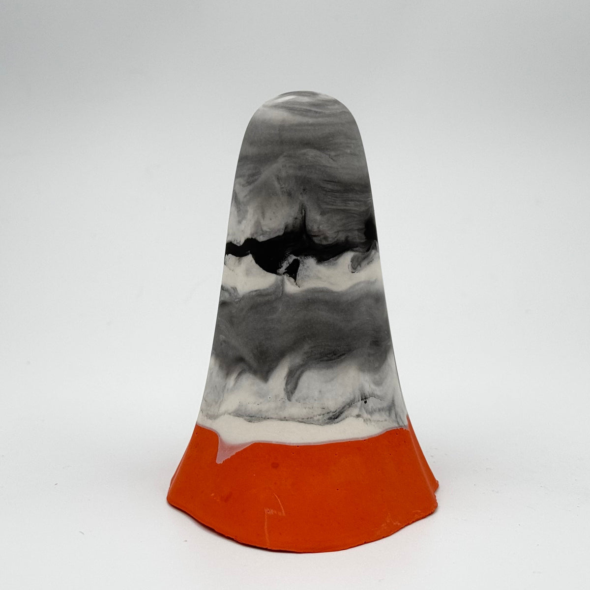 A handmade ghost figurine by The Nordic Ghost Merchants. The body of the ghost is a mix of smoky charcoals and whites. At the base is a small band of pumpkin orange. Rear view on a grey studio background.