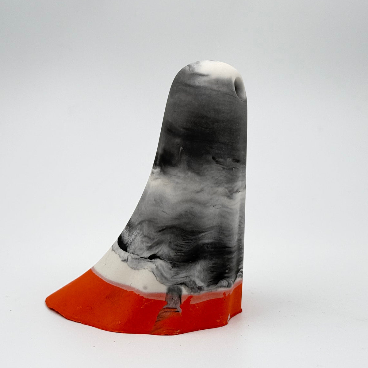 A handmade ghost figurine by The Nordic Ghost Merchants. The head and body of the ghost are a misty or smoky mix of grey and white. The bottom portion is a pumpkin orange shade. Side view on a grey studio background.