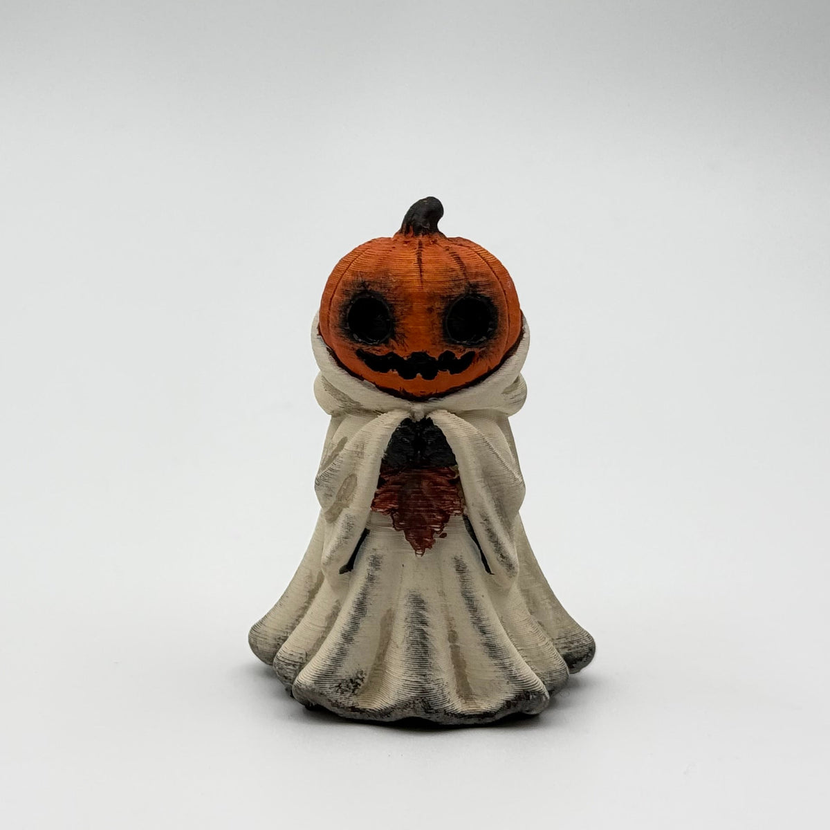 A hand painted folklore figurine made by The Nordic Ghost Merchants in Denmark. The figurine has a carved pumpkin head and is robed in cream cloth while he clutches an autumn leaf. Front view on a grey studio background.