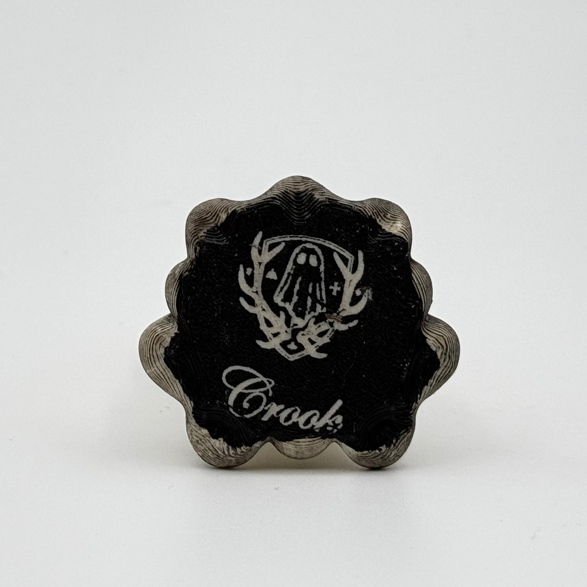 A hand painted folklore figurine made by The Nordic Ghost Merchants in Denmark. The view is of the base of the ornament, painted black and engraved the brand logo - a sheet ghost inside of a coat of arms.