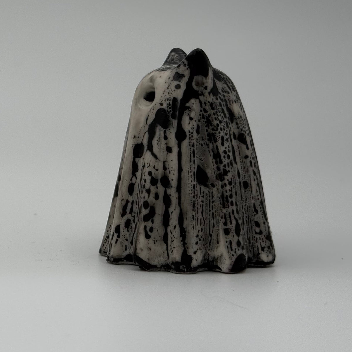 An ivory ghost cat figurine with dramatic black, bark like patterning, made by The Nordic Ghost Merchants. Side view.