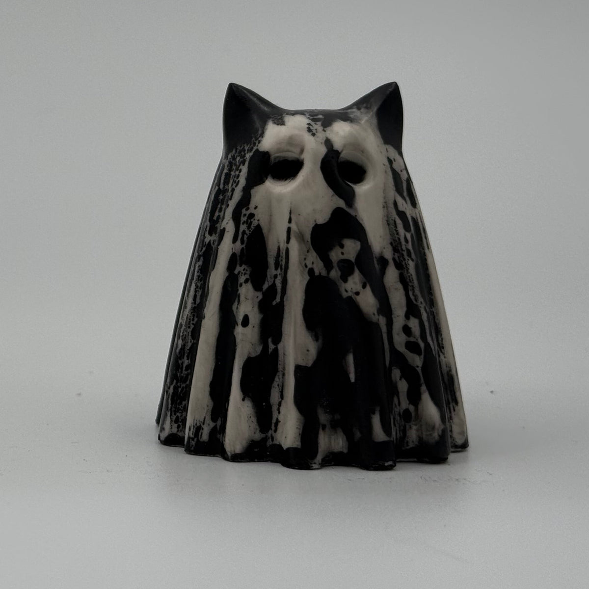 An ivory coloured ghost cat figurine with dramatic black, bark like patterning made by The Nordic Ghost Merchants. Front view.
