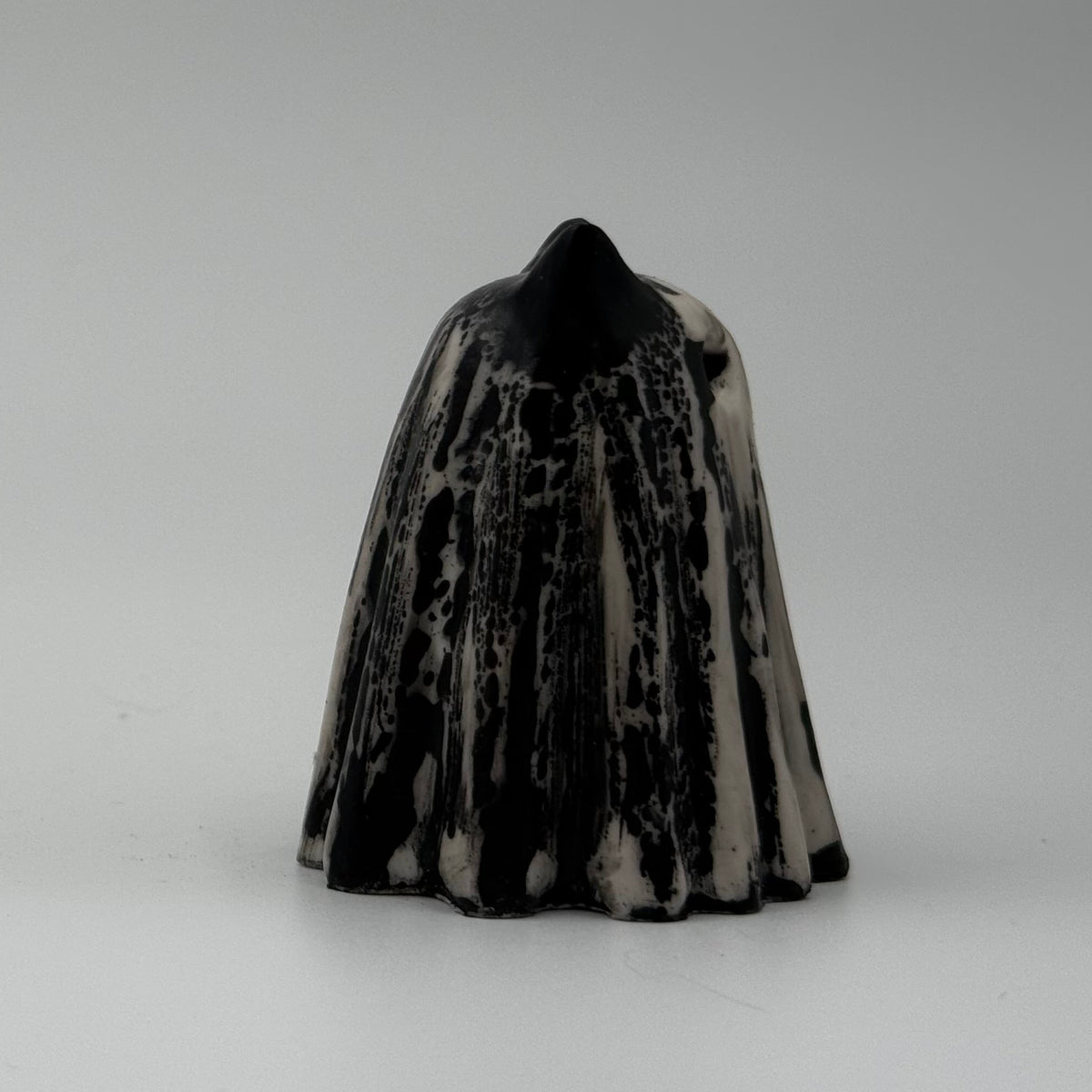 An ivory coloured ghost cat figurine with dramatic black, bark like patterning made by The Nordic Ghost Merchants. Side view.