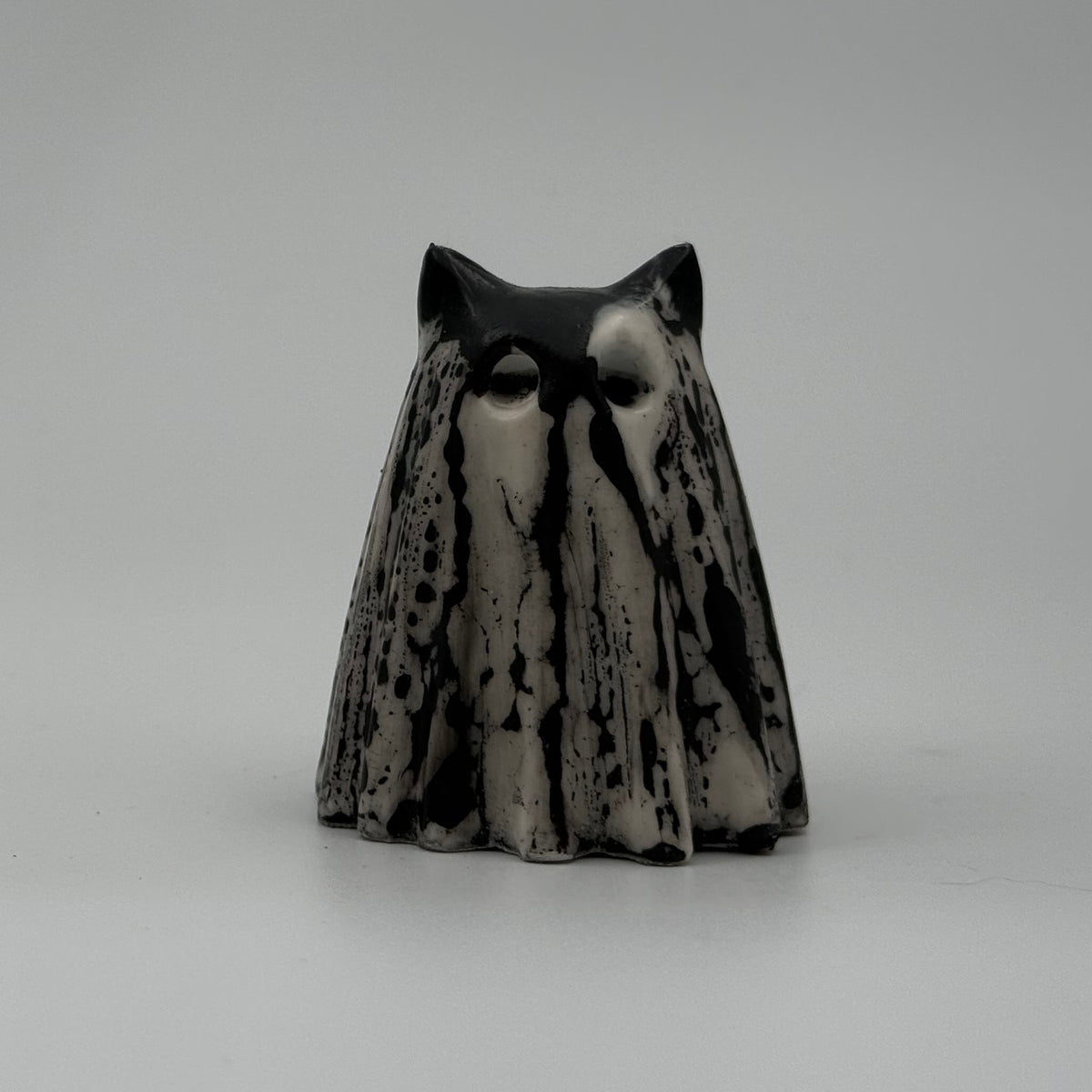 A small black and white ghost cat figurine handmade by The Nordic Ghost Merchants. The pattern resembles rain running down a window. Front view