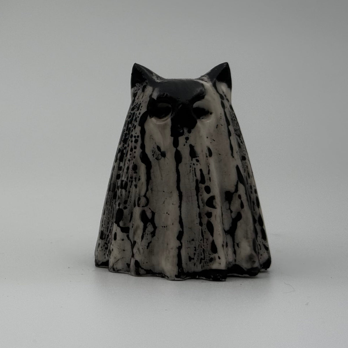 A small black and white ghost cat figurine. The black marks resemble rain dripping down a window. Handmade by The Nordic Ghost Merchants. Front view.