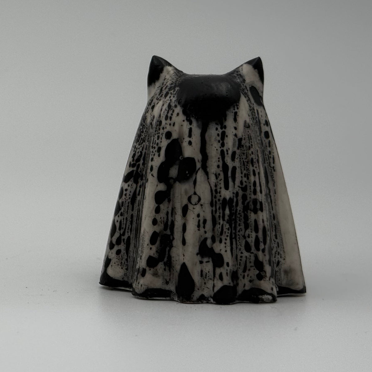 A small black and white ghost cat figurine. The black marks resemble rain dripping down a window. Handmade by The Nordic Ghost Merchants. Rear view.