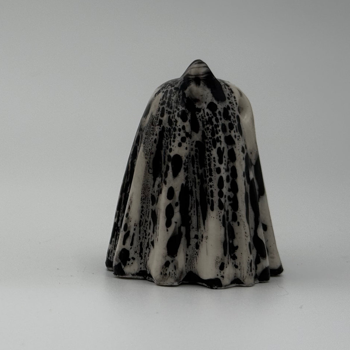 An ivory coloured ghost cat figurine with dramatic black, bark like patterning, made by The Nordic Ghost Merchants. Side view.