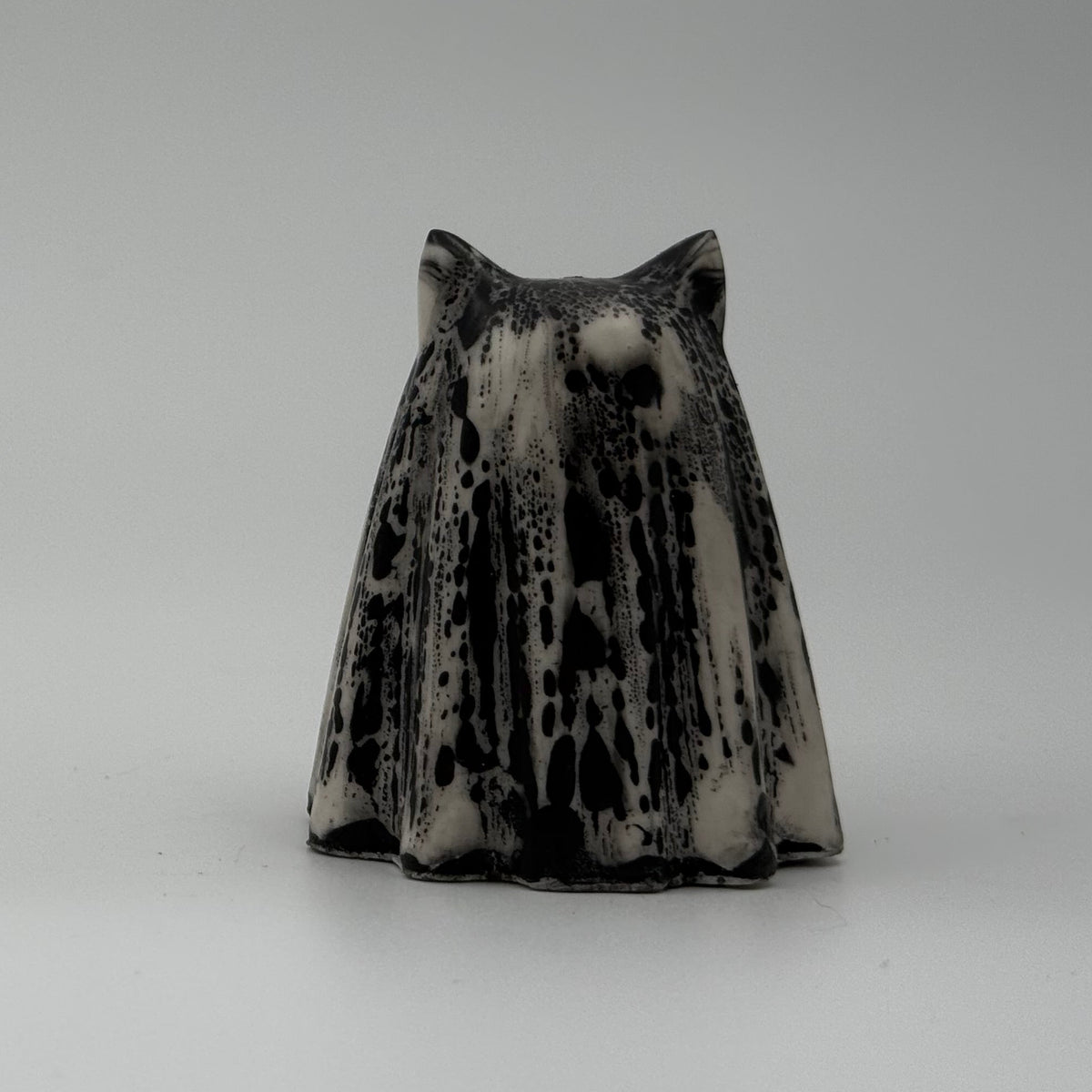 An ivory coloured ghost cat figurine with dramatic black, bark like patterning, made by The Nordic Ghost Merchants. Rear view.