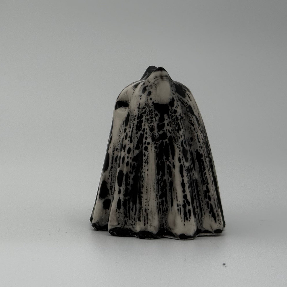 An ivory coloured ghost cat figurine with dramatic black, bark like patterning, made by The Nordic Ghost Merchants. Side view.