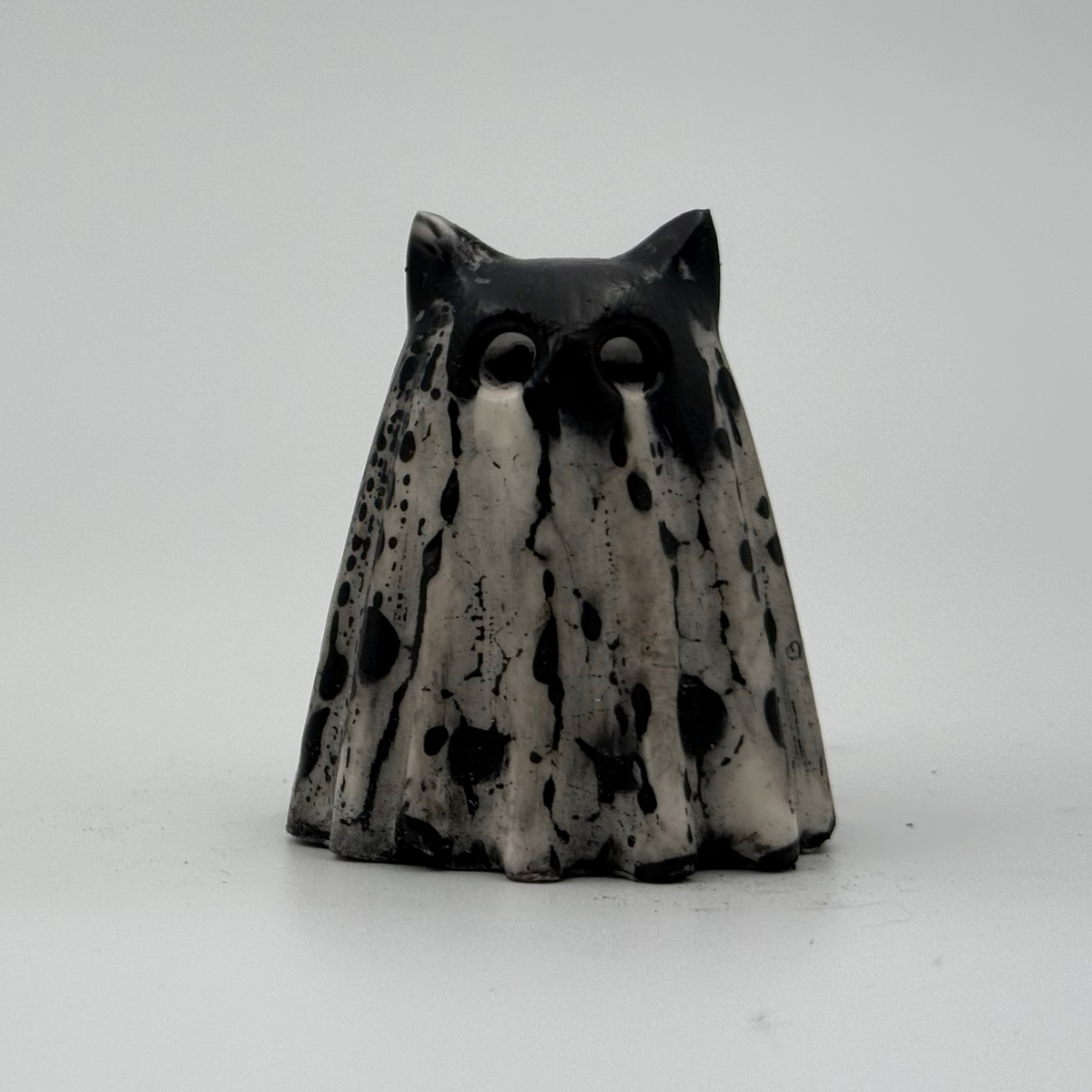 A small black and white ghost cat figurine made by The Nordic Ghost Merchants. Front view.