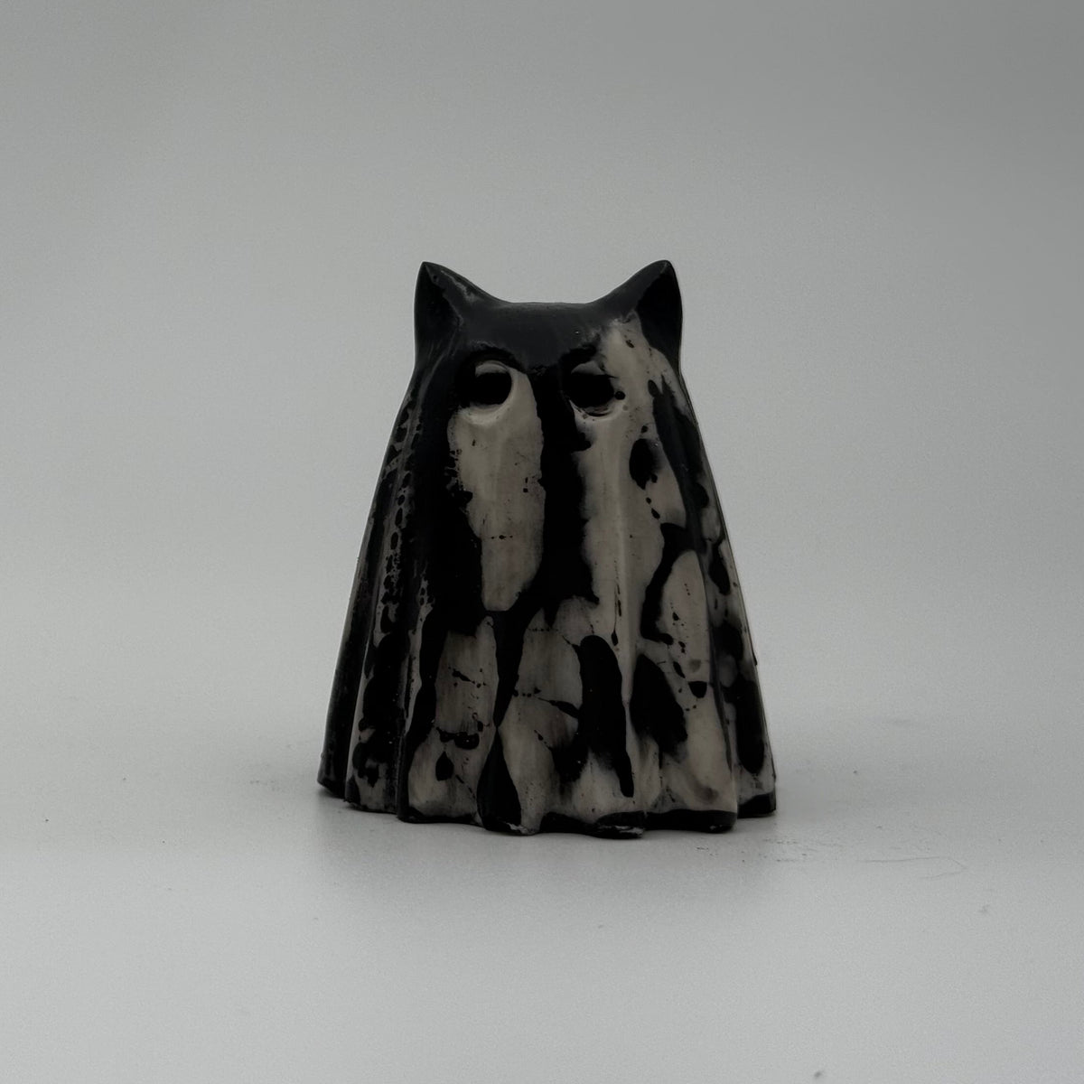A small black and white ghost cat figurine made by The Nordic Ghost Merchants. The pattern resembles bark. Front view.