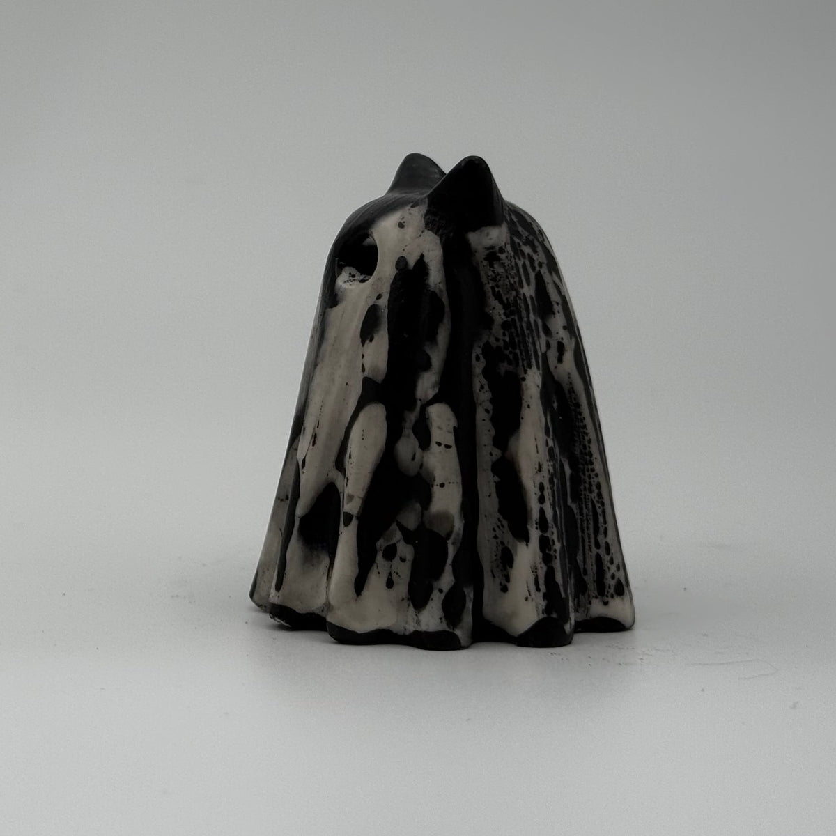 A small black and white ghost cat figurine made by The Nordic Ghost Merchants. The pattern resembles bark. Side view.