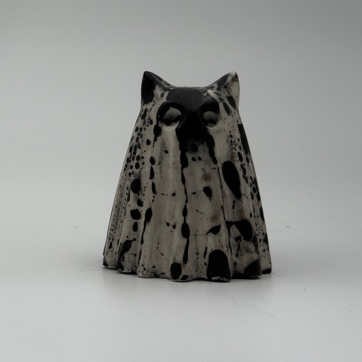 An ivory ghost cat ornament with dramatic black, bark link patterning, made by The Nordic Ghost Merchants. Front view.