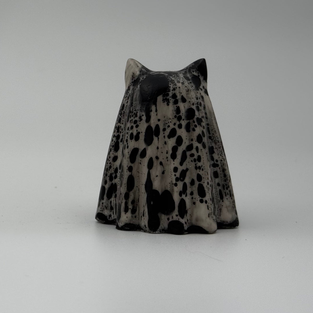 An ivory ghost cat ornament with dramatic black, bark link patterning, made by The Nordic Ghost Merchants. Rear view.