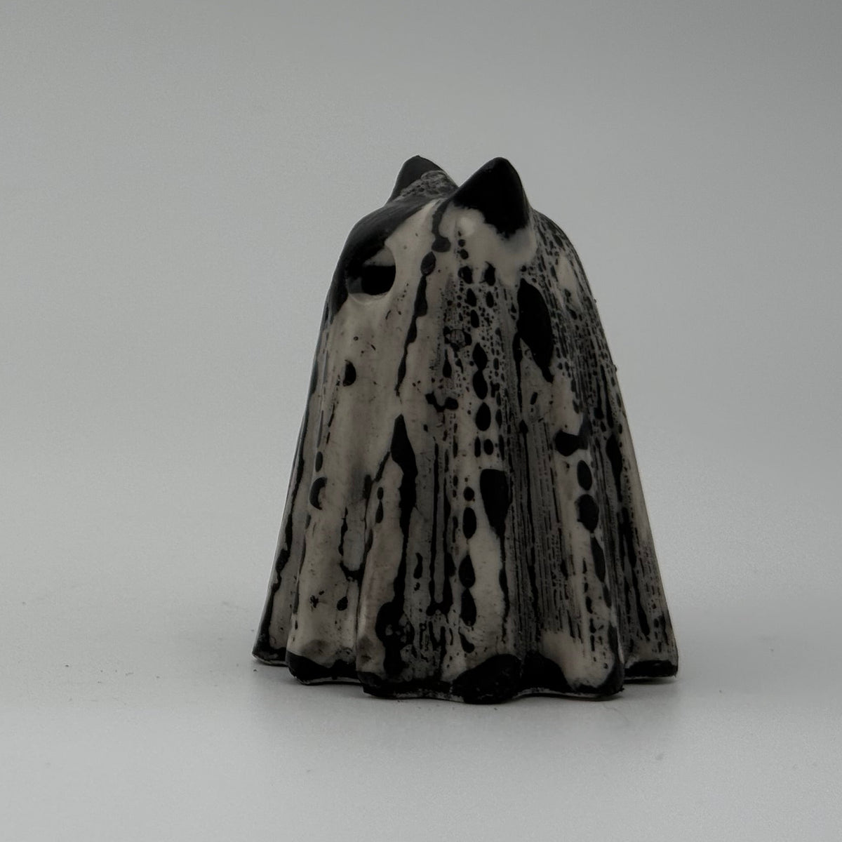 A small black and white ghost cat figurine. The black marks resemble rain dripping down a window. Handmade by The Nordic Ghost Merchants. Side view.