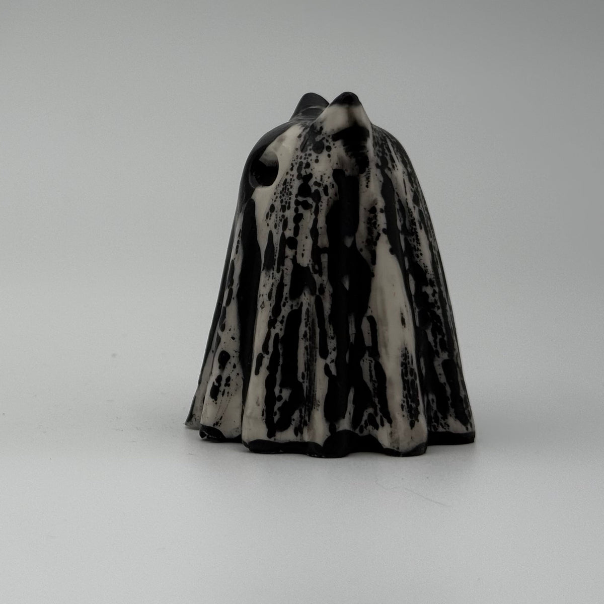 An ivory coloured ghost cat figurine with dramatic, black, bark like patterning, made by The Nordic Ghost Merchants. Side view