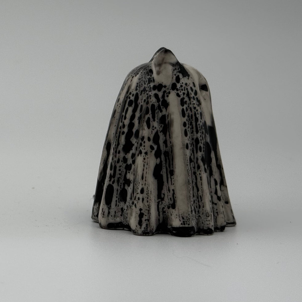 An ivory ghost cat figurine with dramatic black, bark like patterning, made by The Nordic Ghost Merchants. Side view.