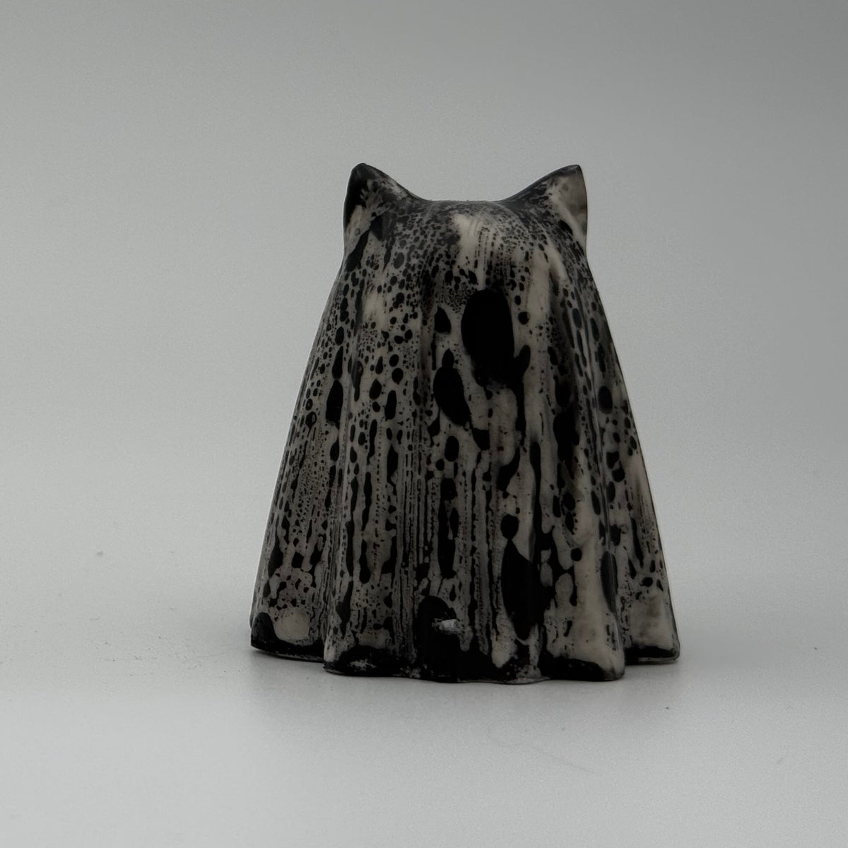 An ivory ghost cat figurine with dramatic black, bark like patterning, made by The Nordic Ghost Merchants. Rear view.