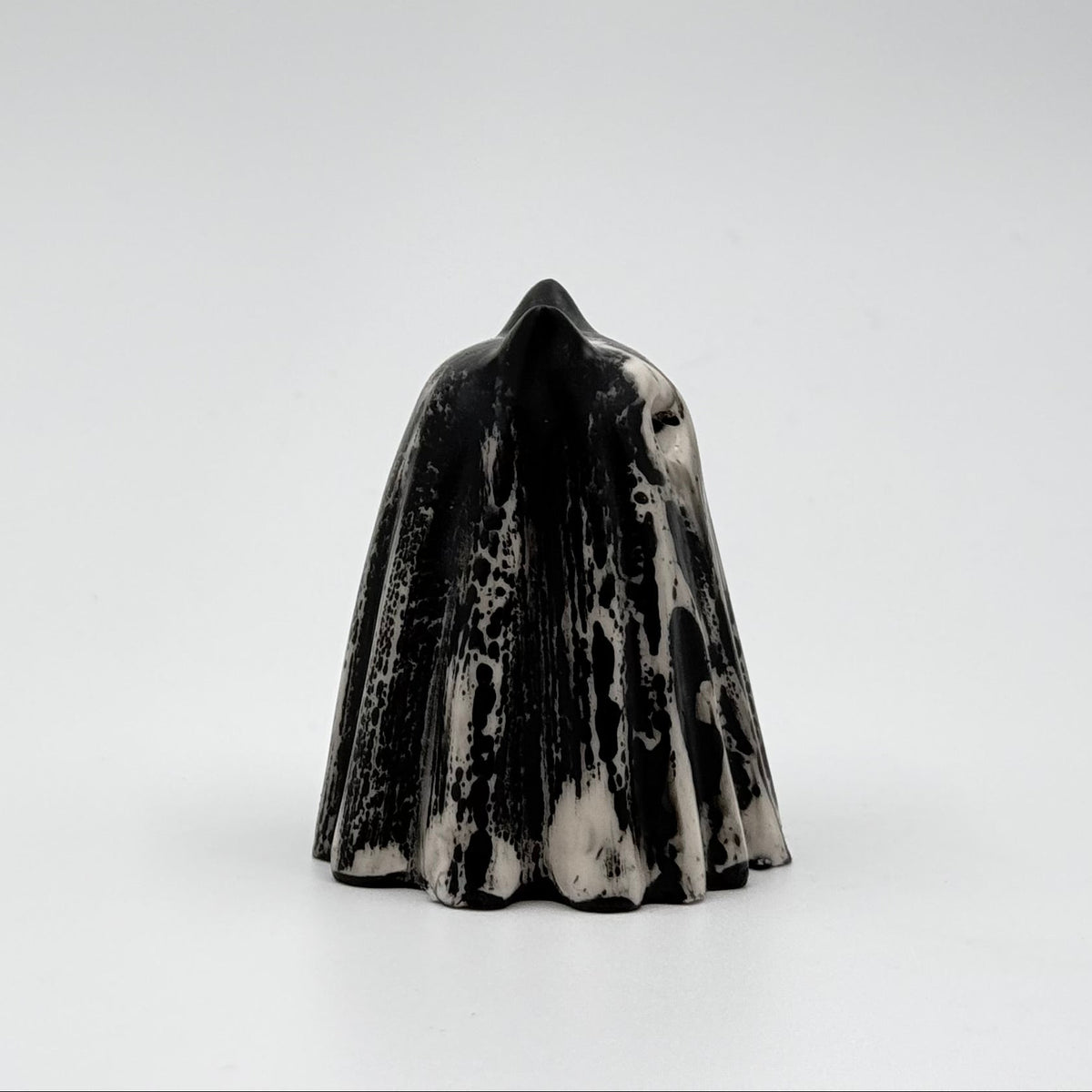A handmade ghost cat figurine made by The Nordic Ghost Merchants. The ghost ornament is bone white with black, bark like patterning. Side view on a grey studio background.