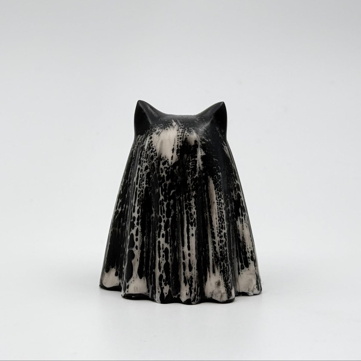 A handmade ghost cat figurine made by The Nordic Ghost Merchants. The ghost ornament is bone white with black, bark like patterning. Rear view on a grey studio background.