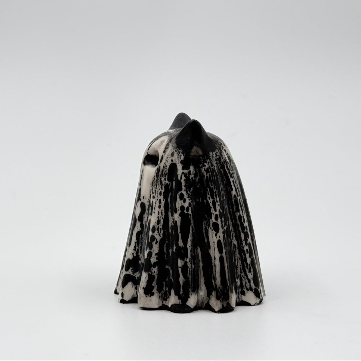 A handmade ghost cat figurine made by The Nordic Ghost Merchants. The ghost ornament is bone white with black, bark like patterning. Side view on a grey studio background.