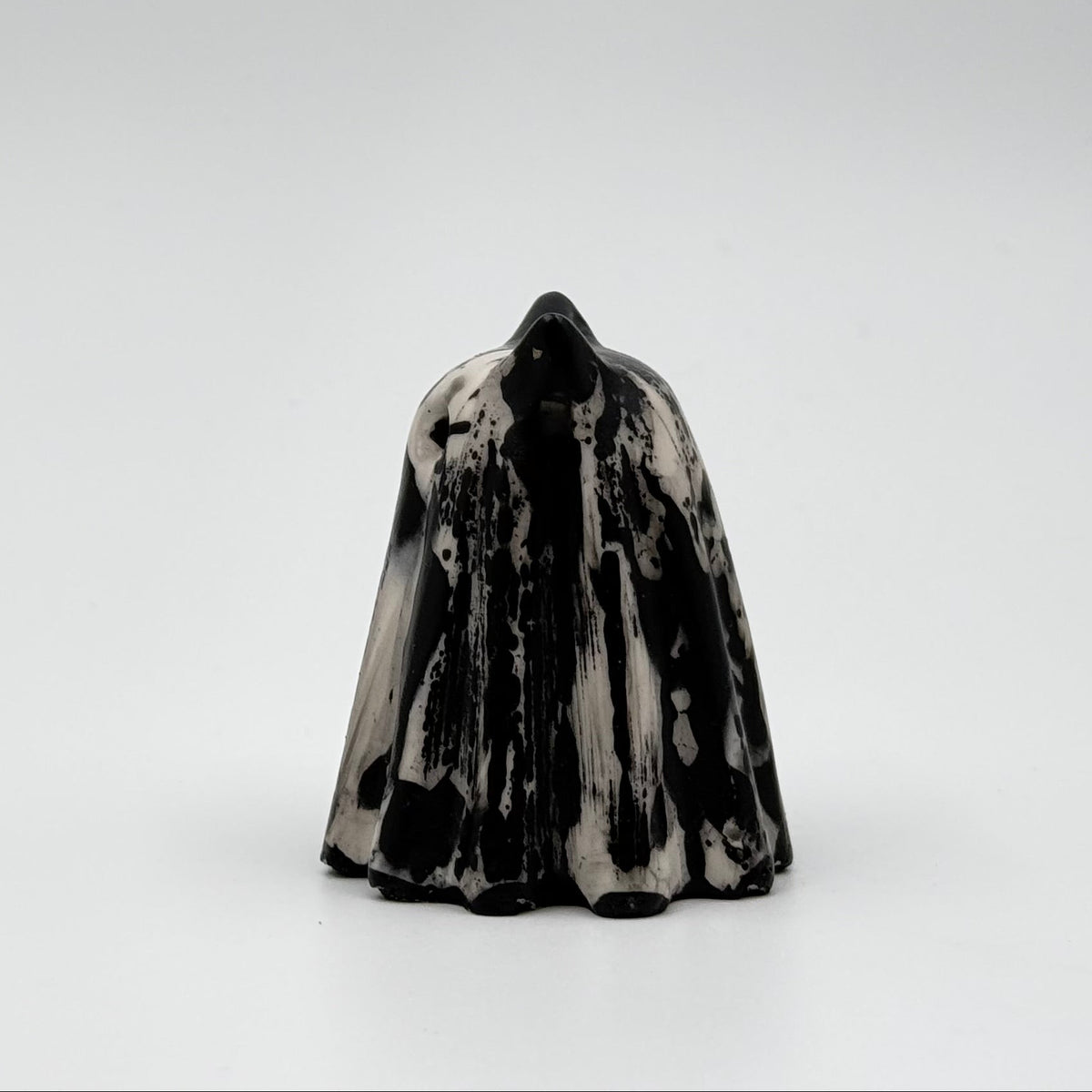 A handmade ghost cat figurine by The Nordic Ghost Merchants. The ghost ornament is bone white with black, bark like patterning. Side view on a grey studio background.